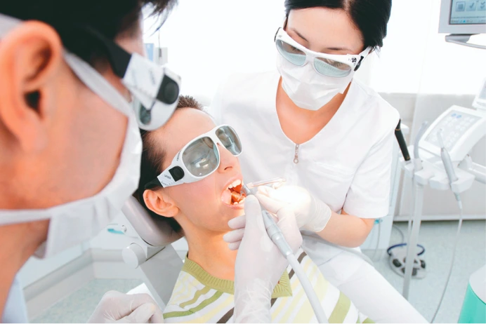 Zahnärzteteam bei der Arbeit mit Laserbehandlung; Patient trägt Schutzbrille, um die Augen vor dem Laserlicht zu schützen.