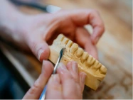 Handwerkliche Bearbeitung eines Zahnmodells aus Gips mit einem feinen Werkzeug, das die Herstellung einer Zahnkrone zeigt.