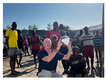 Dr. Drescher übergibt einen Fußball an Kinder während eines gemeinnützigen Projekts in Afrika – soziales Engagement auf der Seite Soziales Engagement.